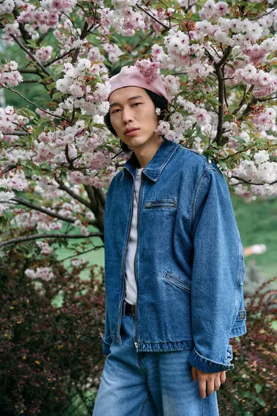 A young asian man stands confidently in a trendy denim outfit, surrounded by vibrant blooms. — Stock Photo