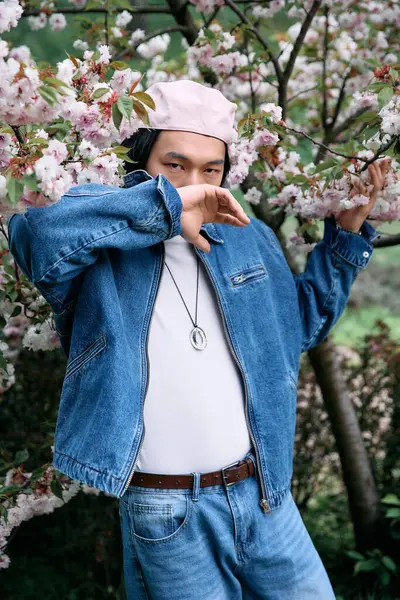 A young man dressed in trendy denim enjoys the beauty of nature in a park filled with blossoms. — Stock Photo
