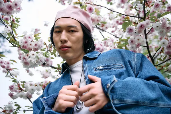 In a vibrant park, a young Asian man showcases a chic denim outfit against blooming flowers. — Stock Photo