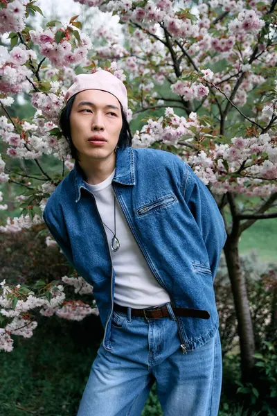 A young asian man enjoys a peaceful moment in a park, showcasing his trendy denim ensemble. — Stock Photo