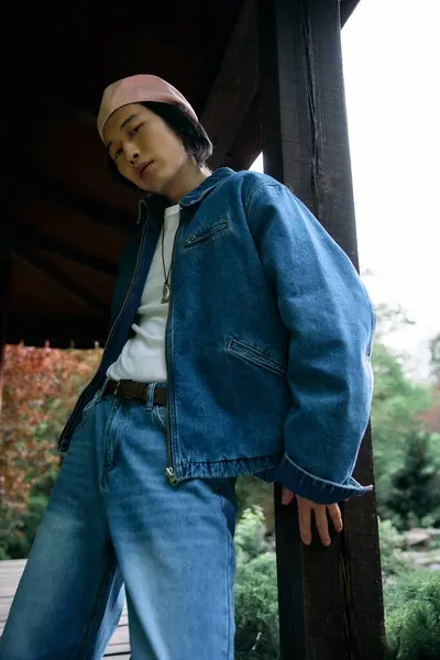 Un joven asiático muestra su traje de mezclilla de moda mientras se relaja en un exuberante entorno de parque. - foto de stock