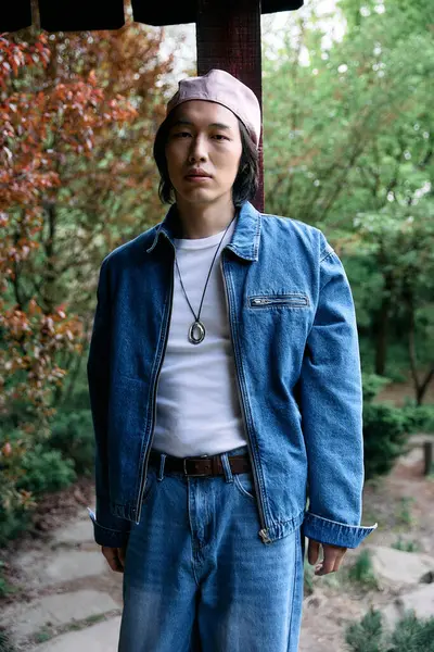 Un joven asiático muestra un look denim de moda mientras está de pie en un entorno de parque. - foto de stock