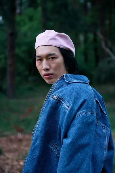 Young man showcases a trendy denim outfit and pink cap, enjoying the peaceful park atmosphere. — Stock Photo