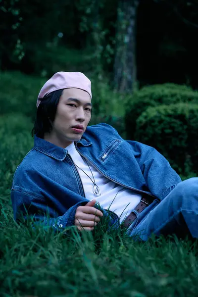 A young asian man relaxes in the park, showcasing his stylish denim outfit under natural light. — Stock Photo