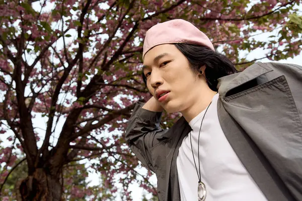 A young man showcases his fashionable grey trench coat while enjoying a spring day in the park. — Stock Photo