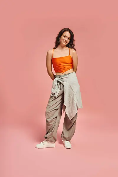 Confident young woman in trendy attire poses against a pink backdrop, radiating modern style. — Stock Photo