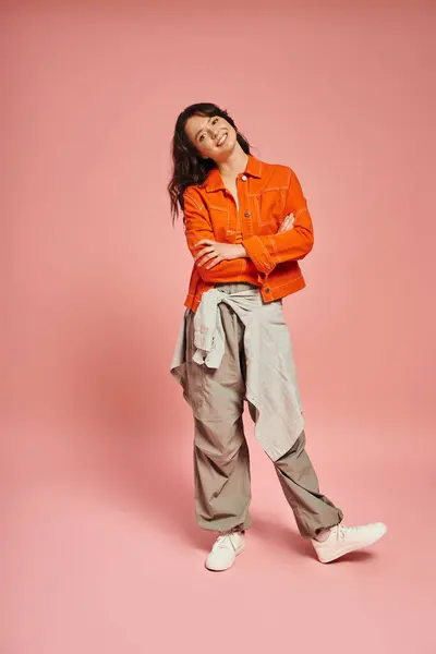 Fashionable young woman poses playfully against a soft pink backdrop, showcasing her trendy outfit. — Stock Photo