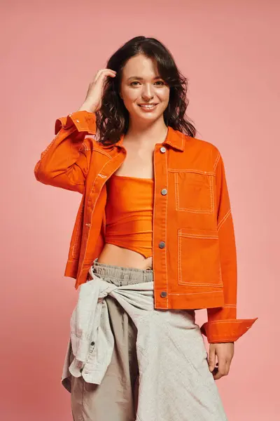 A young woman shows her style in a bright orange jacket and trendy outfit in a lively venue. — Stock Photo