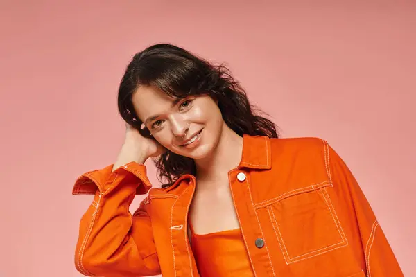 Chic young woman poses playfully in trendy orange attire against a bright pink backdrop. — Stock Photo