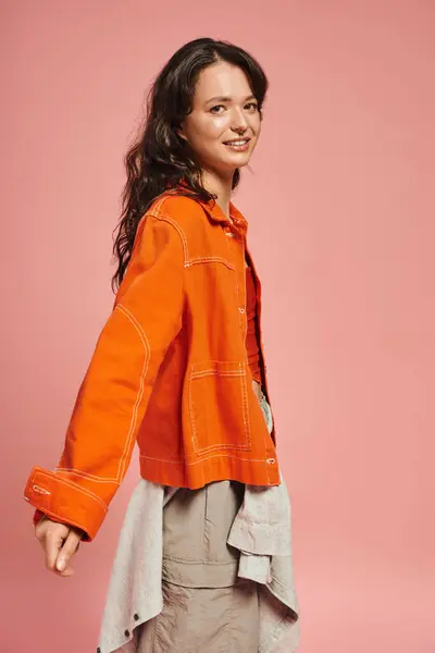 A fashionable young woman showcases her bright orange jacket with a charming smile, radiating style. — Stock Photo