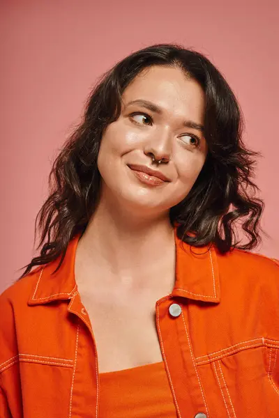 Young fashionable woman smiles playfully while posing in a bright orange attire and a pink backdrop — Stock Photo