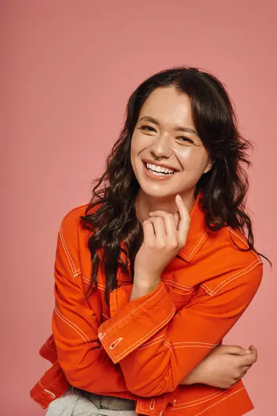 A young woman with a bright smile poses in stylish orange outfits against a pink backdrop. — Stock Photo