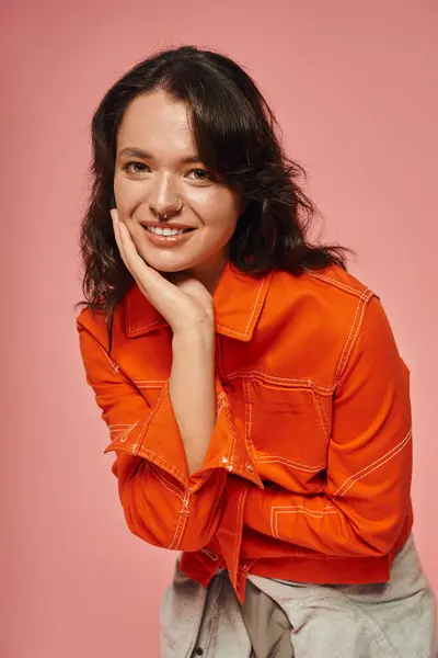 A young woman smiles in a stylish orange outfit, glowing in soft lighting. — Stock Photo