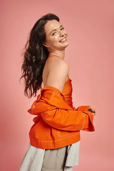 A young woman in fashionable attire smiles joyfully while posing against a bright pink background. — Stock Photo