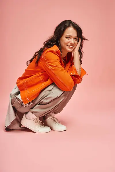 Charming young woman poses joyfully in fashionable orange and gray clothing with a playful smile. — Stock Photo