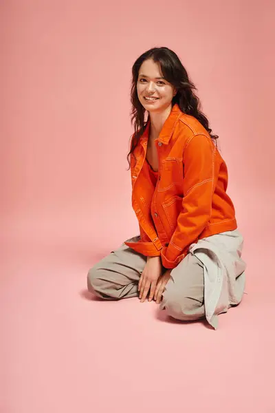 Young woman sits gracefully in a trendy outfit, radiating confidence against a soft pink backdrop. — Stock Photo