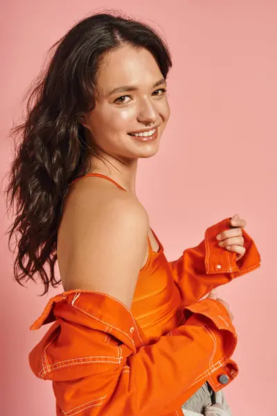 A confident young woman smiles in a trendy outfit against a bright pink backdrop. — Stock Photo