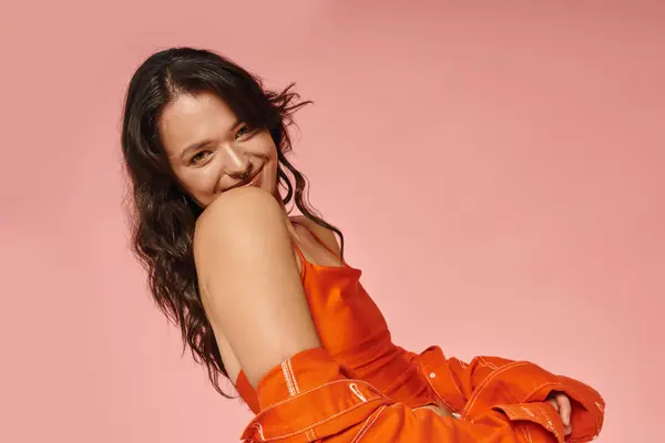 A beautiful young woman confidently showcases her trendy orange attire, radiating joy and style. — Stock Photo
