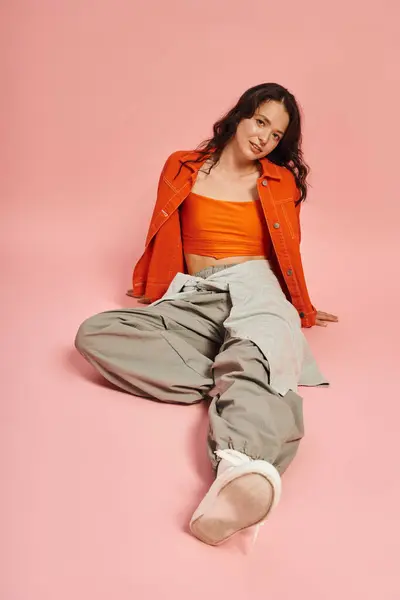 A young woman showcases her chic fashion sense with flair, seated gracefully on a pink backdrop. — стоковое фото