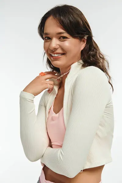 Charming young woman presents her trendy outfit with an inviting smile in a bright space. — Stockfoto