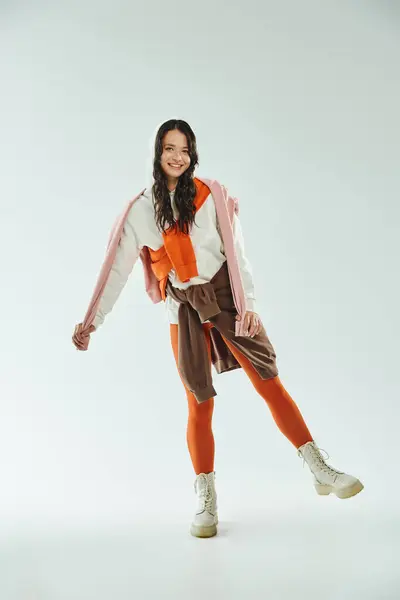 A fashionable young woman strikes a playful pose wearing a vibrant outfit in a bright studio. — Stock Photo