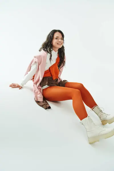 Una giovane donna mostra il suo stile con colori audaci e stivali chic mentre si siede con grazia. — Foto stock