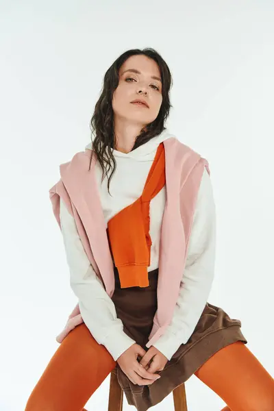 Eine stilvolle Frau sitzt auf einem Hocker und präsentiert ihren einzigartigen Look in einem minimalistischen Raum. — Stockfoto