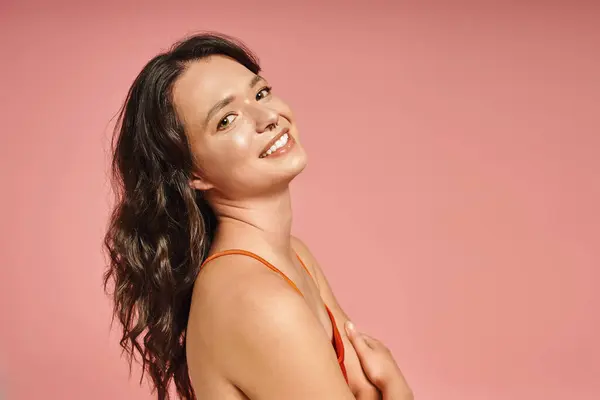 Young woman in fashionable attire smiles confidently while posing against a soft pink background. — стоковое фото