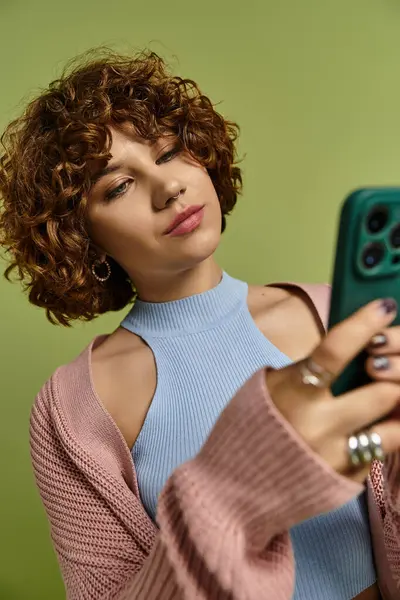 Una mujer joven con el pelo rizado corto muestra un traje de moda mientras usa su teléfono. - foto de stock