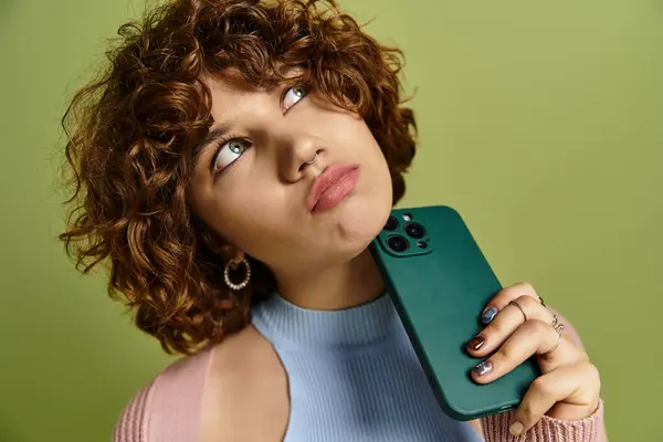 A young woman holding her phone against a vibrant green backdrop. — Stock Photo