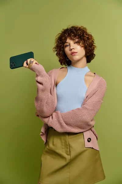 A young woman with short curly hair poses stylishly in a trendy outfit, holding smartphone — Stock Photo