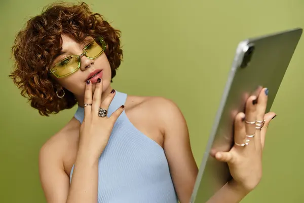 A young woman with short curls poses with tablet in hand, dressed in a stylish summer outfit. — Stock Photo
