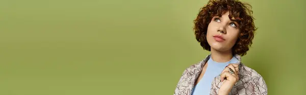 A young woman with curly hair poses in a stylish summer outfit against a green backdrop, banner — Stock Photo
