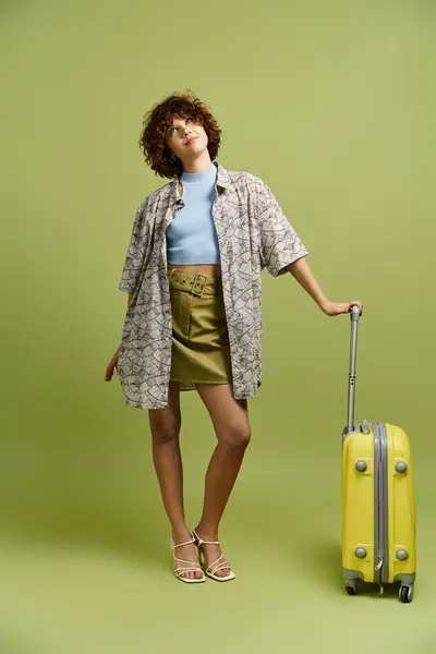 A young woman with curly hair models a summer outfit by a vibrant suitcase. — Stock Photo