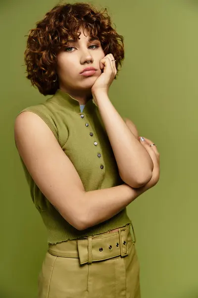 A young woman with short curls poses confidently in a fashionable outfit against a green background. — Stock Photo