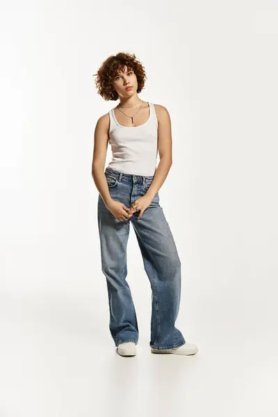 A young woman poses confidently in a tank top and jeans against a clean white background. — Stock Photo