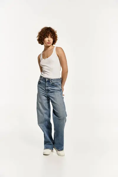 Young woman with short curly hair poses confidently in a casual tank top and jeans. — Stock Photo
