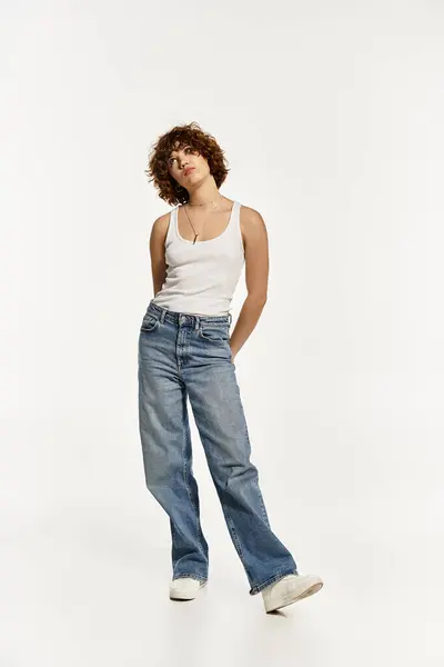 Una mujer joven con el pelo rizado corto posa en una camiseta sin mangas y jeans, exudando vibraciones de moda de verano. — Stock Photo