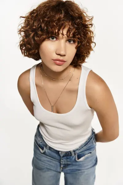 A stylish young woman poses confidently in a tank top and jeans against a white backdrop. — Stock Photo
