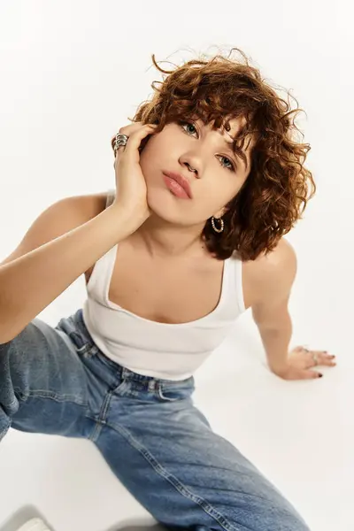 Una mujer joven con rizos cortos posa con estilo en una camiseta sin mangas y jeans sobre un fondo limpio. — Stock Photo