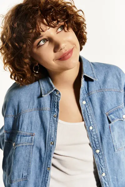 A young woman with short curls poses confidently in a denim shirt on white. — Stock Photo