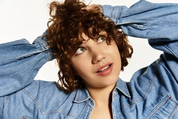 A young woman plays with her curly hair while wearing a fashionable denim shirt — Stock Photo