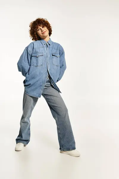 Una joven confiada en una camisa de mezclilla y jeans posa con el pelo rizado corto. — Stock Photo