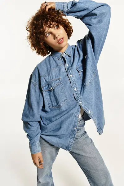 Una mujer joven con el pelo rizado posa con confianza en un traje de mezclilla con estilo, mostrando vibraciones de verano. — Stock Photo