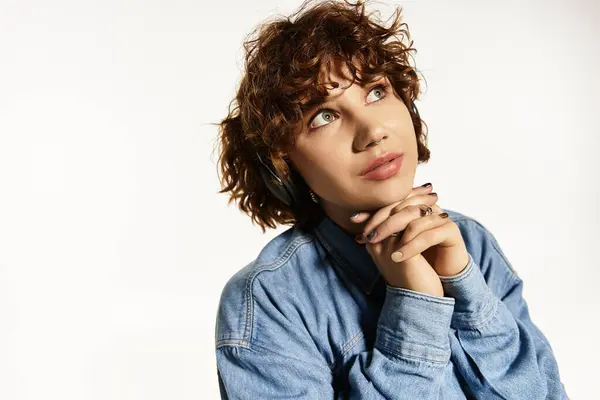 Mujer joven con pelo rizado corto posa en un conjunto de mezclilla chic contra un fondo brillante. — Stock Photo