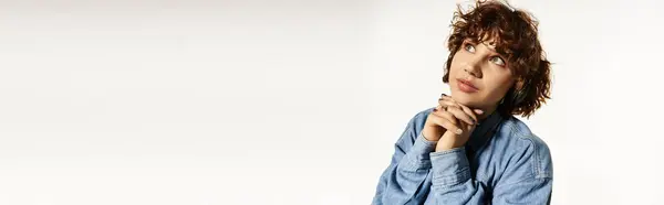 Una joven con el pelo rizado vestido de mezclilla refleja con una expresión reflexiva en su rostro, pancarta — Stock Photo
