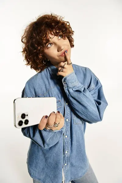A young woman with short curly hair showcases her denim fashion while holding a smartphone. — Stock Photo
