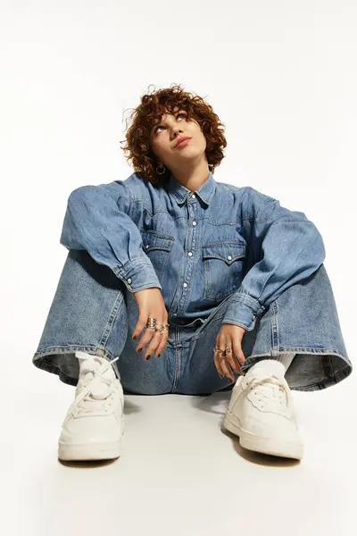 A young woman with short curly hair poses in a stylish denim outfit, radiating confidence. — Stock Photo