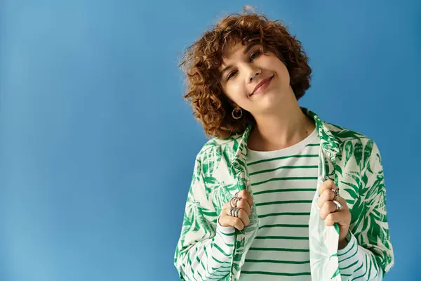 A young woman with curly hair poses confidently in a vibrant outfit against a blue background. — Stock Photo