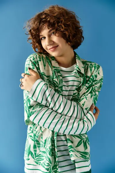 A young woman with short curly hair showcases her vibrant outfit while posing playfully on blue. — Stock Photo